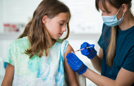 Female nurse with surgical mask and in gloves giving vaccine injection to a child in clinic.