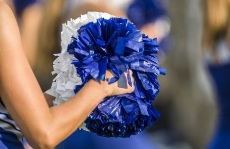 Cheerleader shaking blue and white pom poms.
