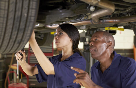 Mechanic and female trainee working underneath car together.