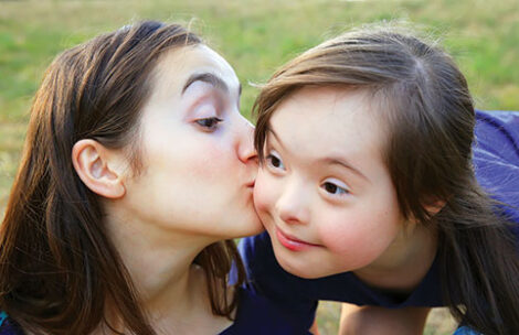 A big sister gives her little sister a kiss on the cheek.