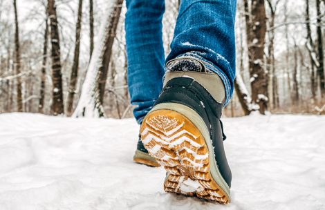 Man's legs in black with orange boots walking in the snow