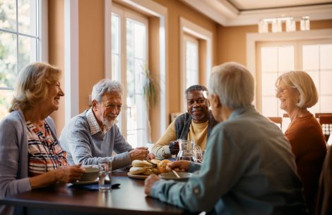 Group of seniors enjoying in conversation during lunch at a dining table in a nursing home.