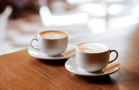 Two cups of cappuccino with latte art on wooden desktop.