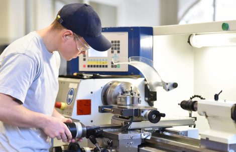 Young apprentice in vocational training working on a turning machine in the industry.