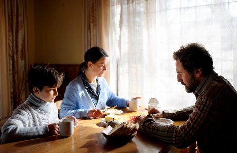 A portrait of poor sad small girl with parents eating indoors at home, poverty concept.