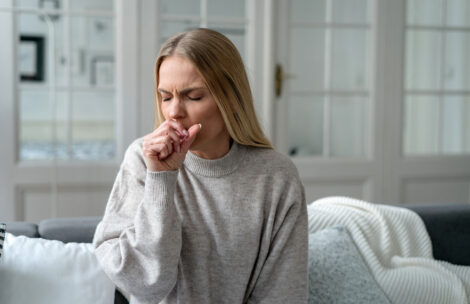 Blonde woman with symptoms of fever and influenza, coughing on her couch.