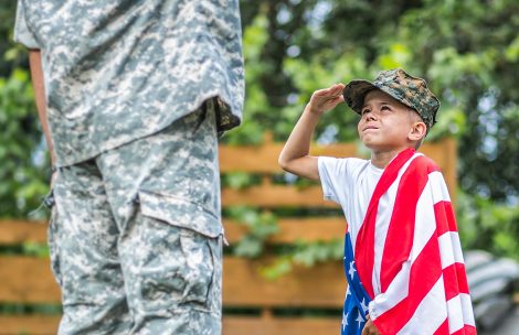 Happy reunion of a soldier with his family. A young boy salutes with an American flag on his shoulder.