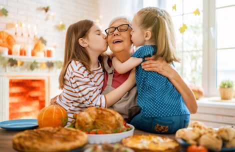 Two granddaughters visit with their grandma for Thanksgiving in front of a table lined with food.