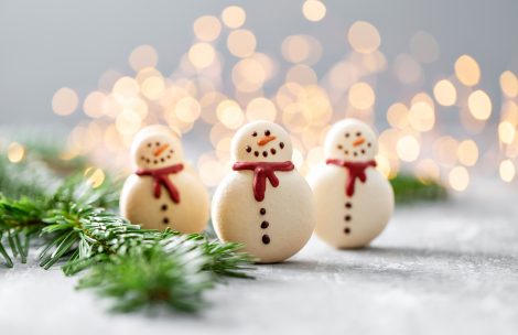 Christmas cookies in the shape of snowmen. Celebrating the winter holidays. Lights and garland appear in the background.