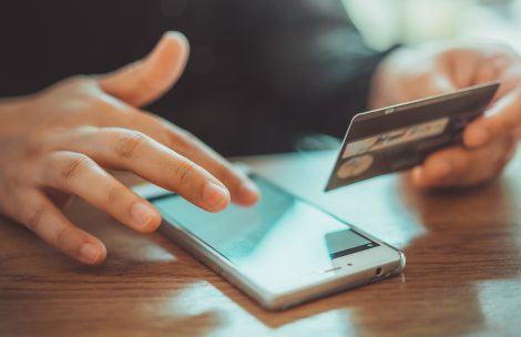 Person responding to a cell phone scam and holding a credit card. Depicts people being tricked into paying a scammer.