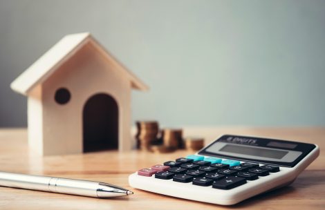 Calculator with wooden house and coins stack and pen on wood table.