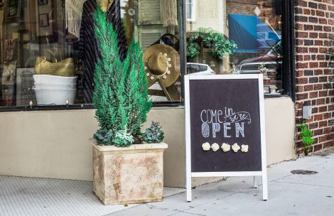 A boutique shop with a sign out front reading "come in, we're open."