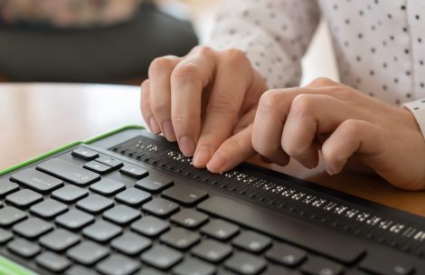 A blind woman uses a computer with a Braille display and a computer keyboard. Inclusive device.