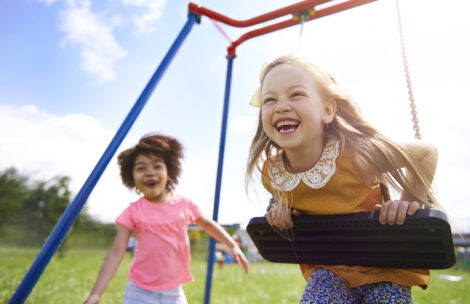 Two child best friends playing together on a swing set.