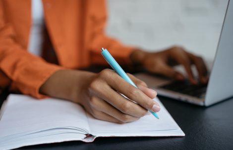 Close-up shot of student hand holding pen and writing in notebook, working at home. E-learning