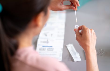 Asian woman using rapid antigen test kit for self test COVID-19 epidemic at home. Adult female place the fabric tip of the swab in the extraction tube and rolling around the tube.