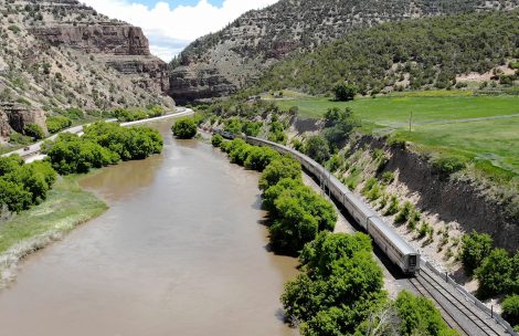 A passenger train climbs eastward following the Colorado River through Glenwood Canyon.