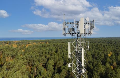 Telecommunication tower with antennas for 5g network on forest and blue sky background.