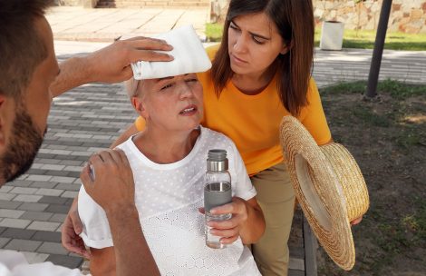 People helping an older adult woman suffering from heat stroke with a bottle of water and a cold rag.