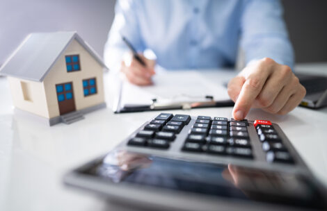 Close-up Of A Person Hand Calculating A Real Estate Property Tax On Wooden Desk.