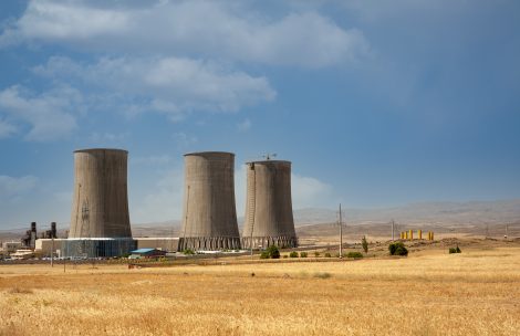 Nuclear power plant cooling towers, big chimneys beside Wheat field with partly cloudy sky.