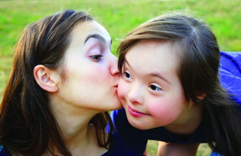 A big sister gives her little sister a kiss on the cheek.