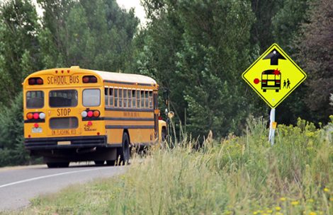 A school bus rides down the road past a bus stop sign.