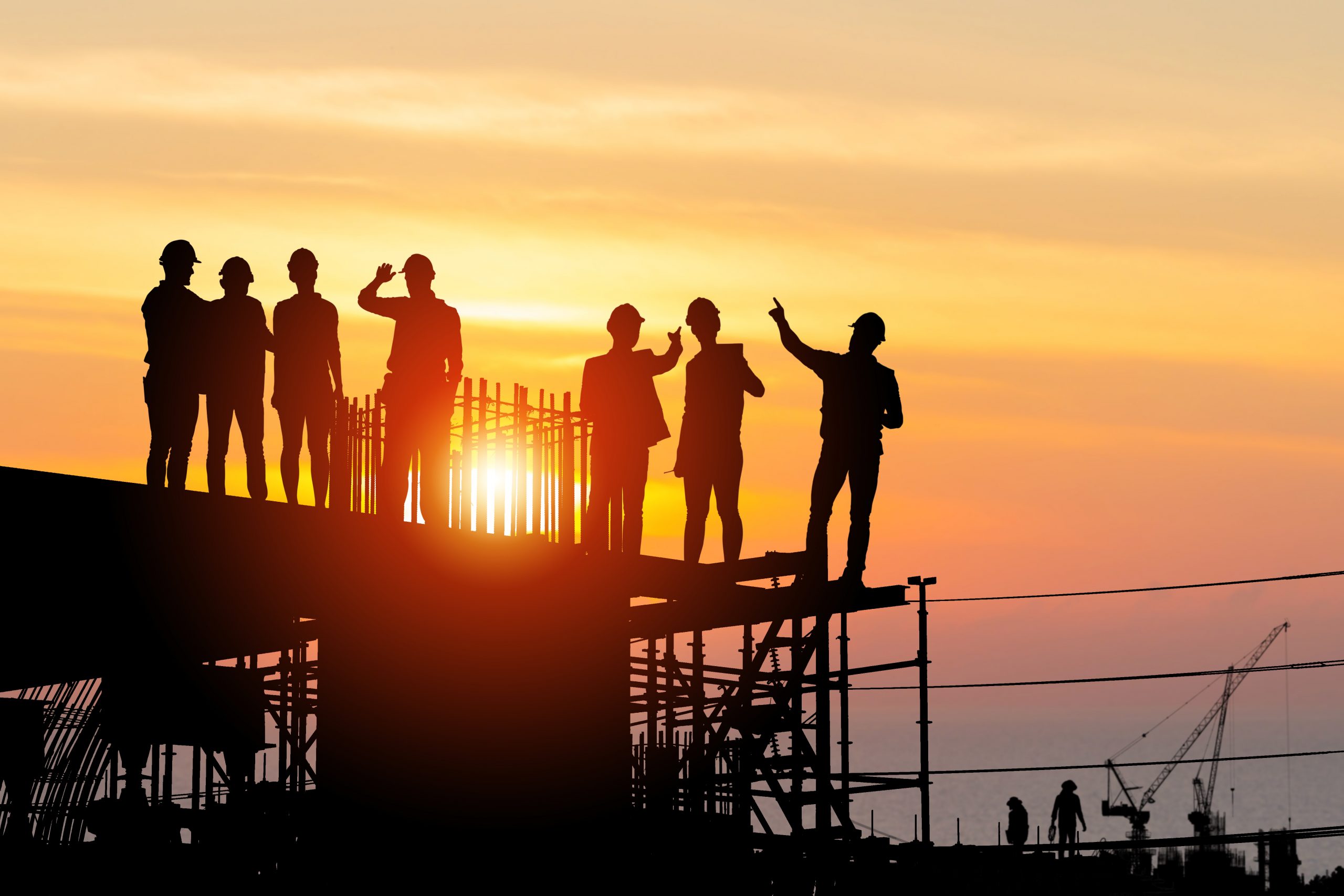 Silhouette of engineer and work team on building site with a bright sunset in the background.