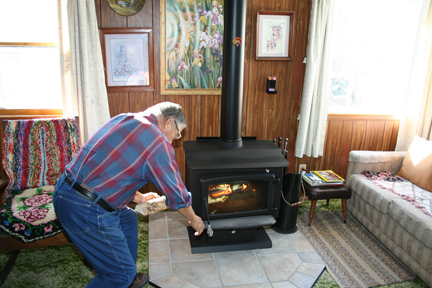 A man adds wood into his woodstove inside his home.